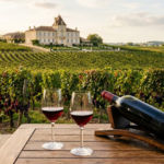 Cánh đồng nho Bordeaux với lâu đài đá, hai ly vang đỏ và chai vang nằm trên giá gỗ