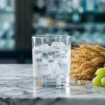 Ly vodka đá lạnh cạnh bông lúa mì, nho xanh và củ khoai tây trên mặt đá cẩm thạch